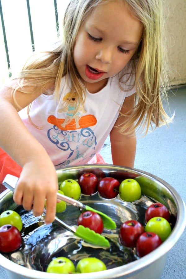 A little girl in front of a bowl of fruit, with Apple and School