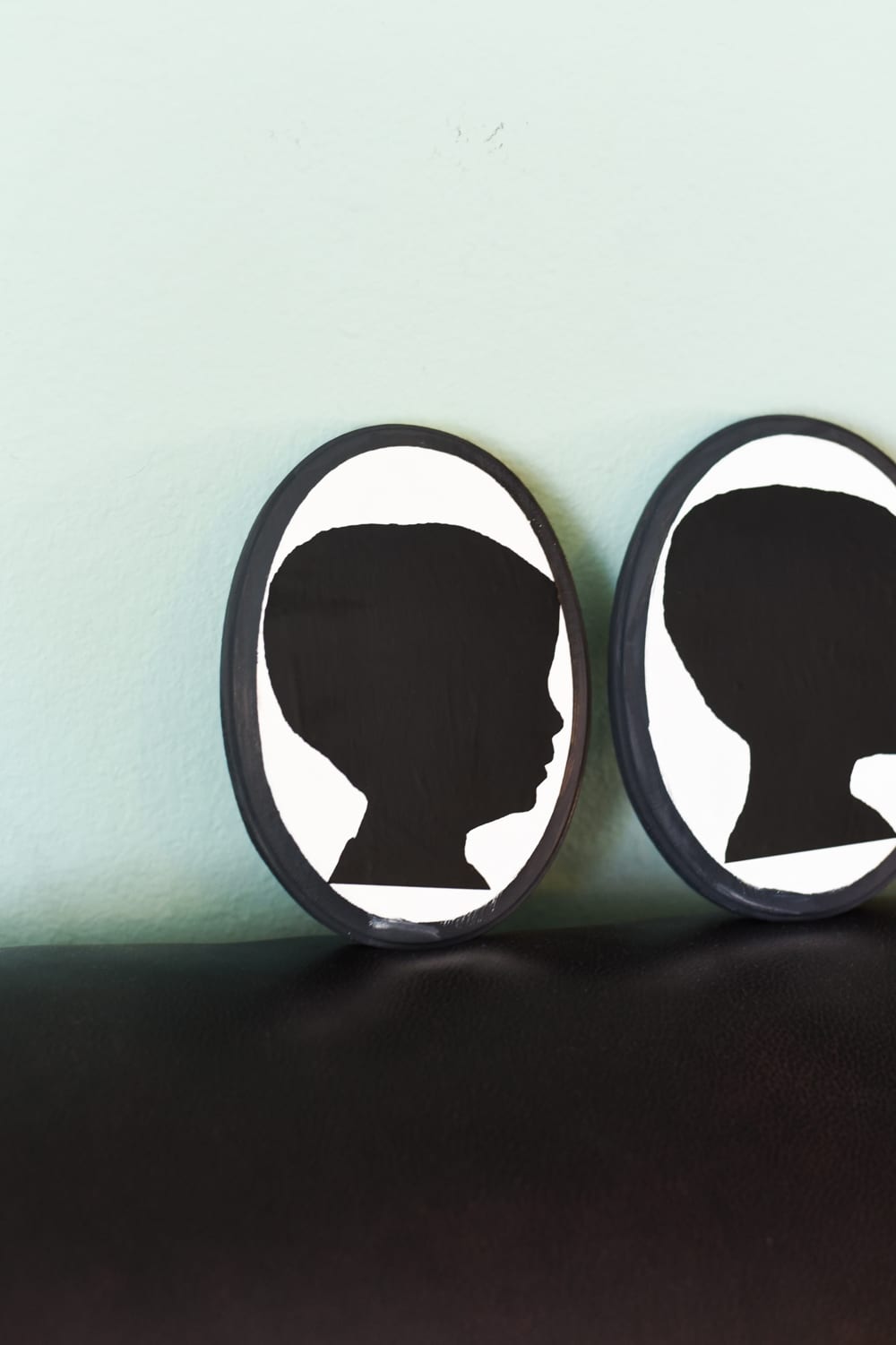 two silhouette portraits on coach by green wall