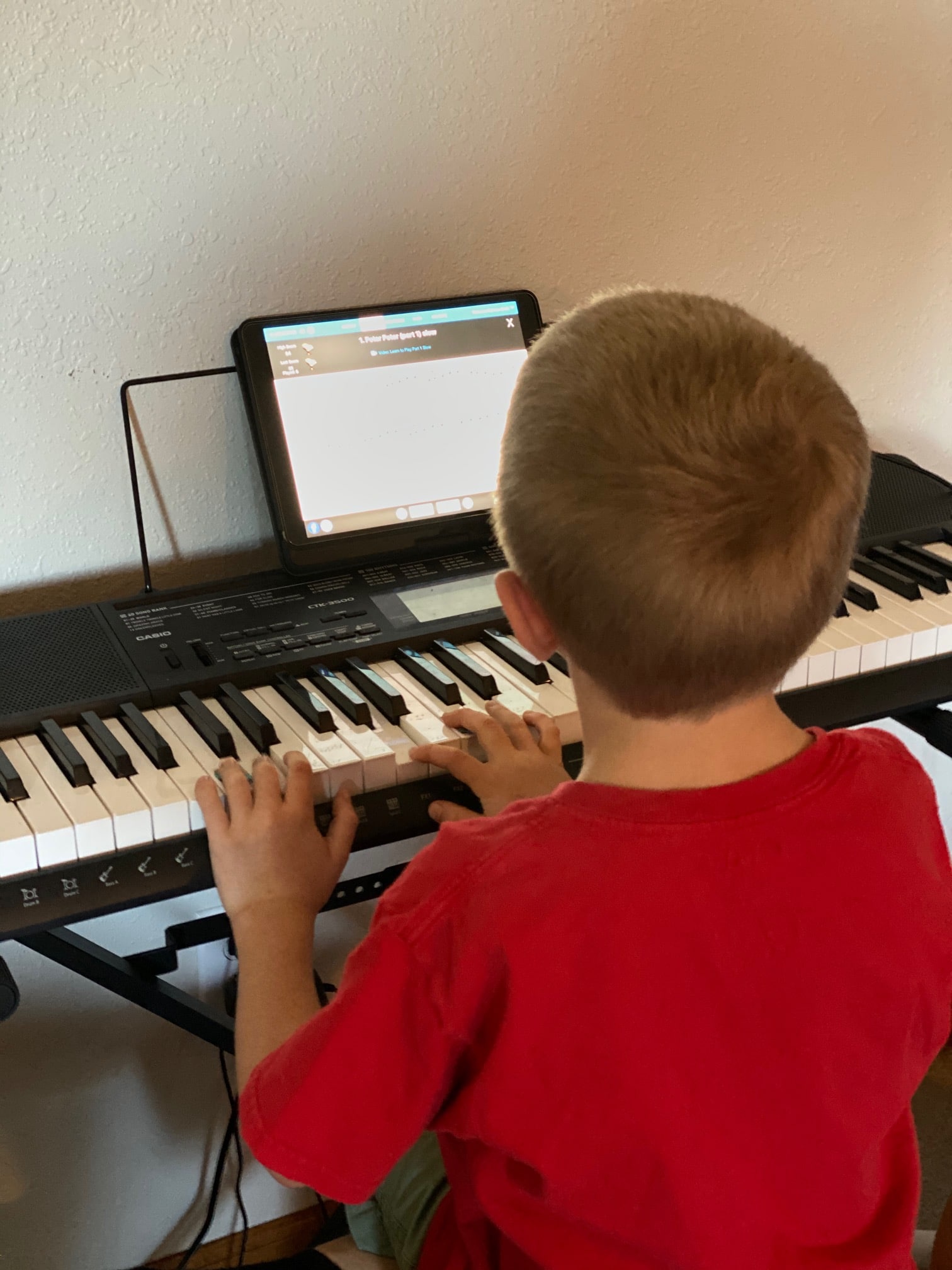 A boy sitting at a desk in front of a piano keyboard playing piano marvel