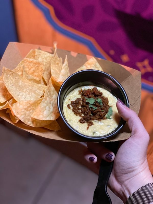 A person holding a plate of nachos with dip